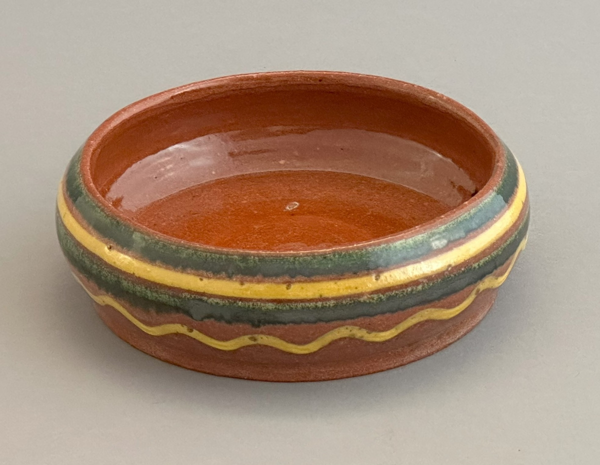 Rödbrun skål av lergods med gul och grön dekor på utsida.