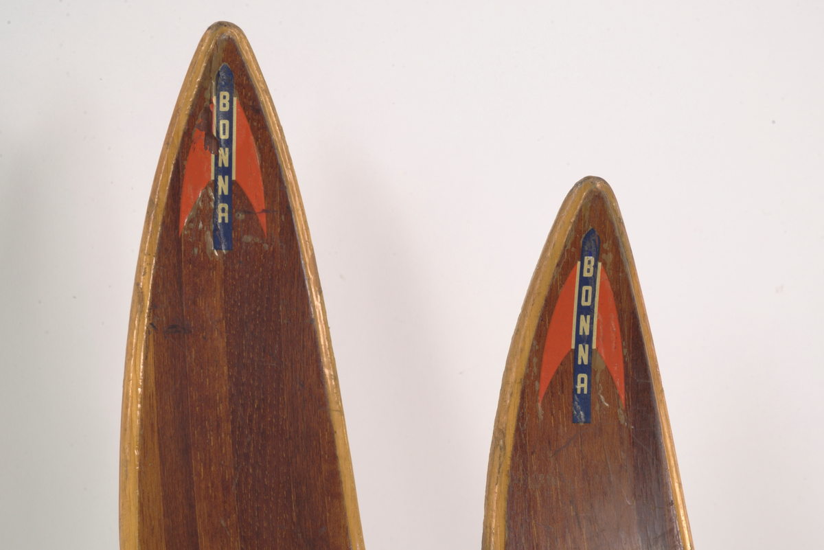 En av et par brune treski (den andre A.06019-01.a) med lysere brune kanter. Laminert tre. Merke på oversiden av skituppen "Bonna" vertikal skrift på blå bakgrunn, røde spisse vinger på hver side av teksten. Rødlakkert Rottefella tåbinding.