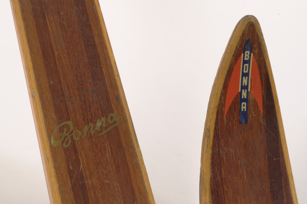 En av et par brune treski (den andre A.06019-01.b) med lysere brune kanter. Laminert tre. Merke på oversiden av skituppen "Bonna" vertikal skrift på blå bakgrunn, røde spisse vinger på hver side av teksten. Rødlakkert Rottefella tåbinding.