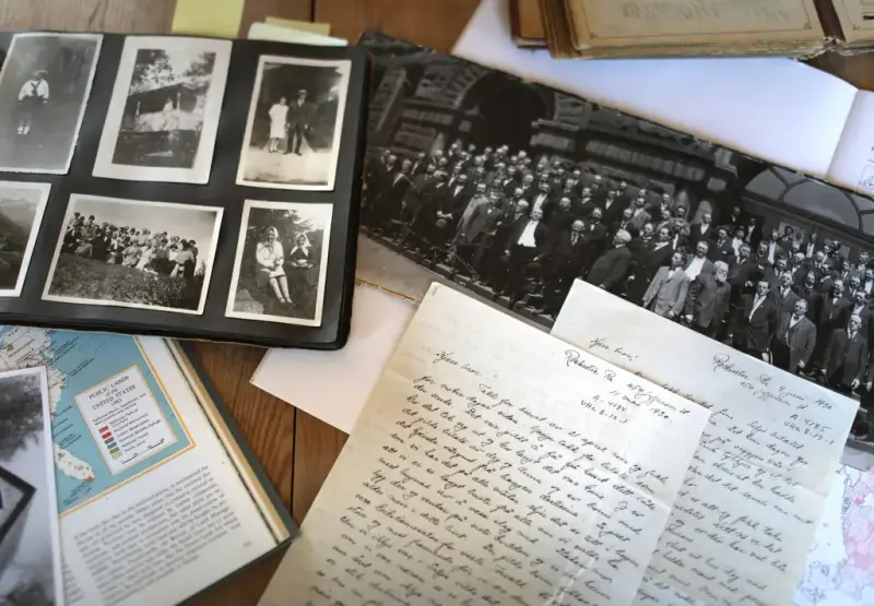 Arkivmateriale på et bord. Fotoalbum med gamle sort-hvit bilder, et større fotografi, to håndskrevne amerikabrev og en bokside med kart.