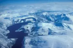 Flyfoto : snøkledde fjell og en innsjø eller vann.