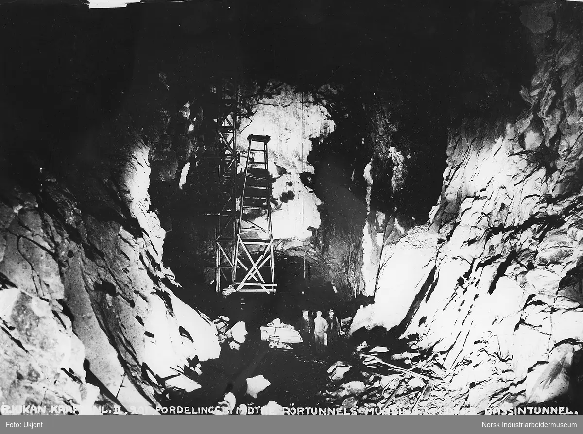 Tre menn, antagelig en ingeniør og to arbeidere stående i munningen på midtre rørtunell til fordelingsbassenget for Såheim kraftstasjon.