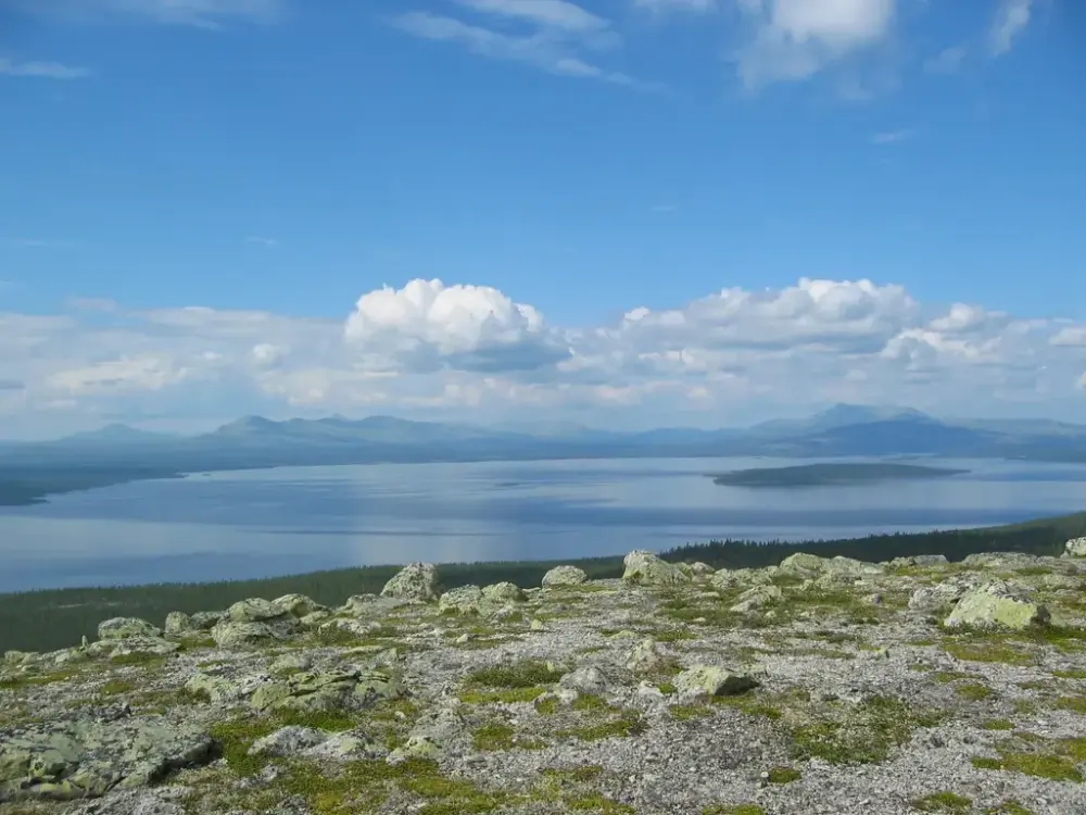 Oversiktsbilde av Femundsmarka nasjonalpark. Sol med noen skyer, sjøen opptar store deler av bildet, og fjell i bakgrunnen