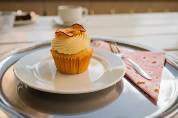 Nærbilde av en muffins med hvit smørkrem og en tørket epleskive på toppen.