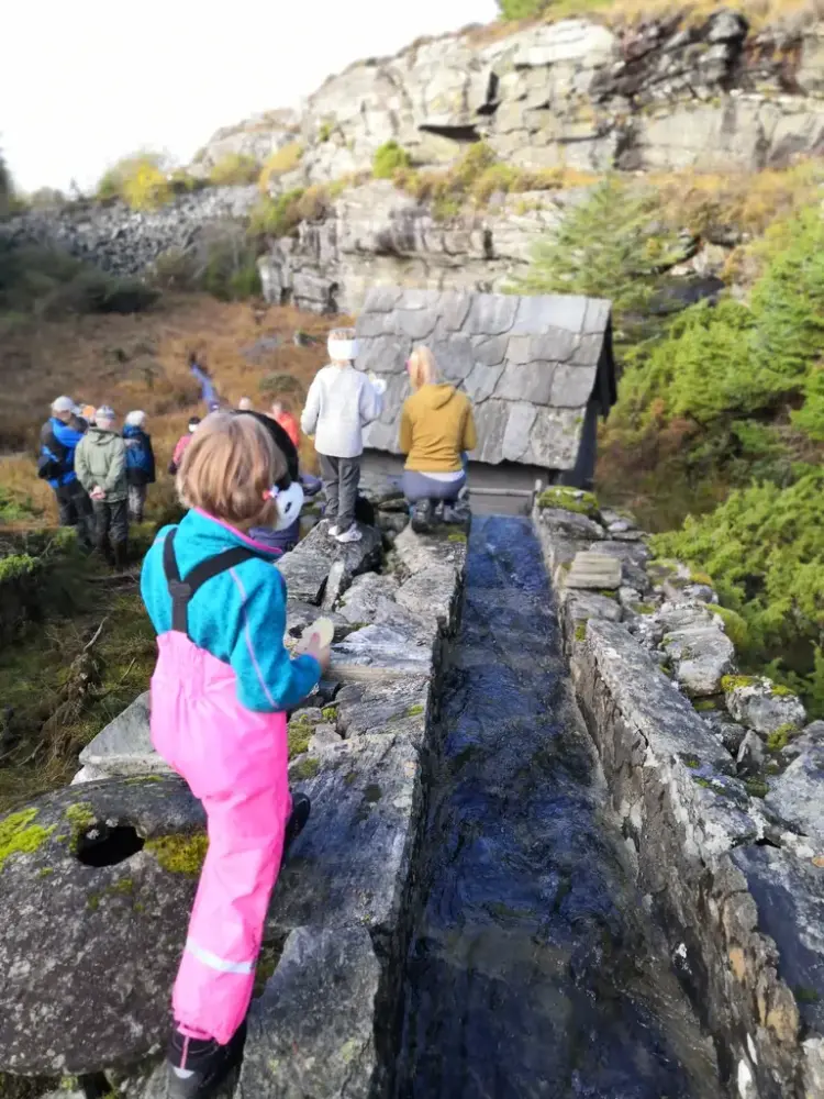 Barn i rosa regnbukse ved en vannrenne. Høst. Kverna i Selstø i Telavåg.