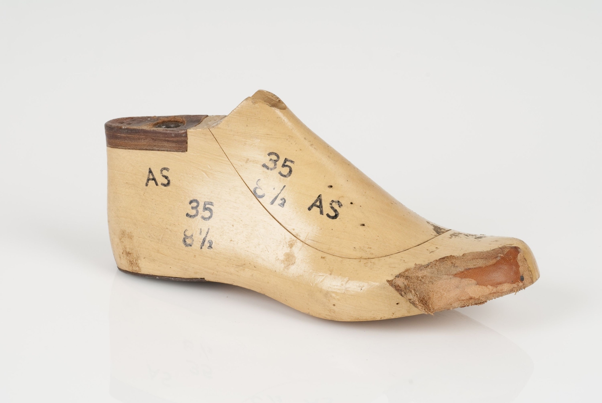 En tremodell i to deler; lest og opplest/overlest (kile).
Høyrefot i skostørrelse 35, og 8,5 cm i vidde.
Lestekam av skinn.
Hælstykke av metall.