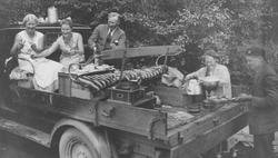 Fem personer har piknik på lasteplanet med mat og vin. Benke