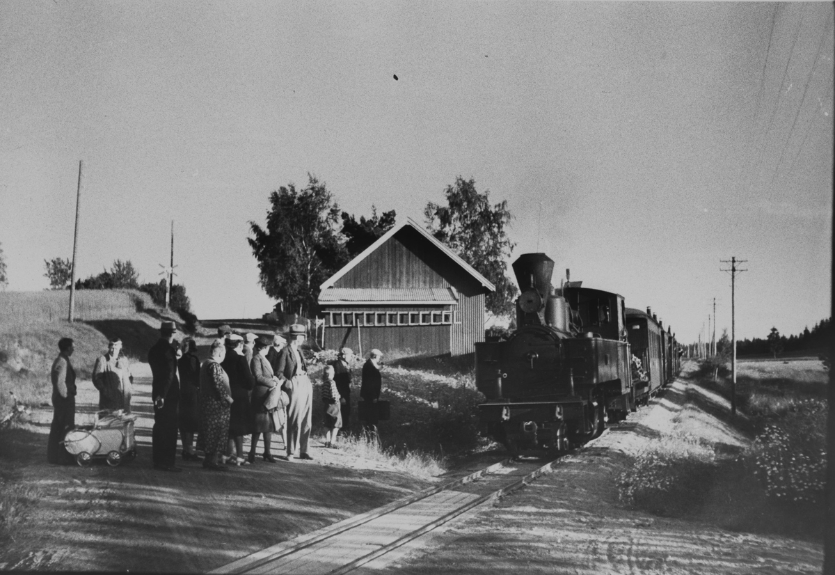 Tog retning Sørumsand stopper for påstigning på Furulund planovergang og holdeplass. Lokomotivet fyres med ved, og frontlykten på lokomotivet er blendet.