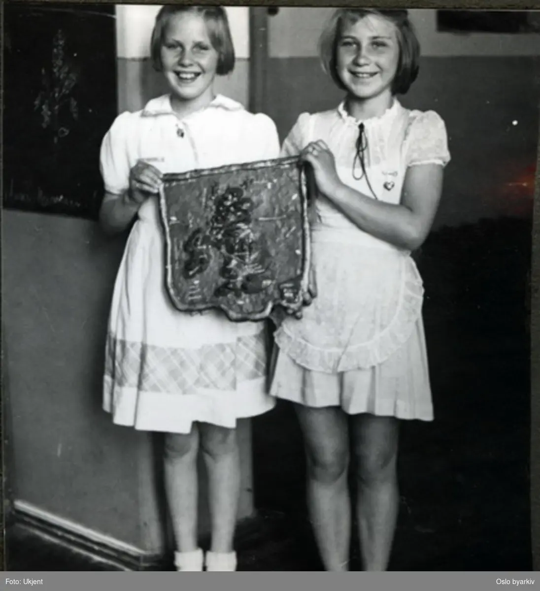 To glade jenter som viser fram sitt relieffkart på skoleutstilling. Albumtittel: "Sofienberg skole femti år - første september 1933."