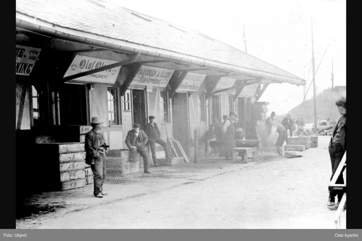Den nye fiskehallen fra 1905. Fiskeforretninger. Grossist-handlere venter på kunder. Tomkasser. Reklame / Skilt. Bildet er datert 23/5-06.