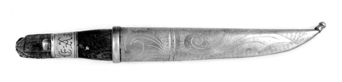 Kniven har brunbeiset skaft, antageligvis av bjørk. Slire og holker er av messing. Slira er foret med papp. Hempa er av imitert krokodilleskinn. Kniven er innkjøpt sammen med andre kniver i ei samling fra Birger Arntzen. 
