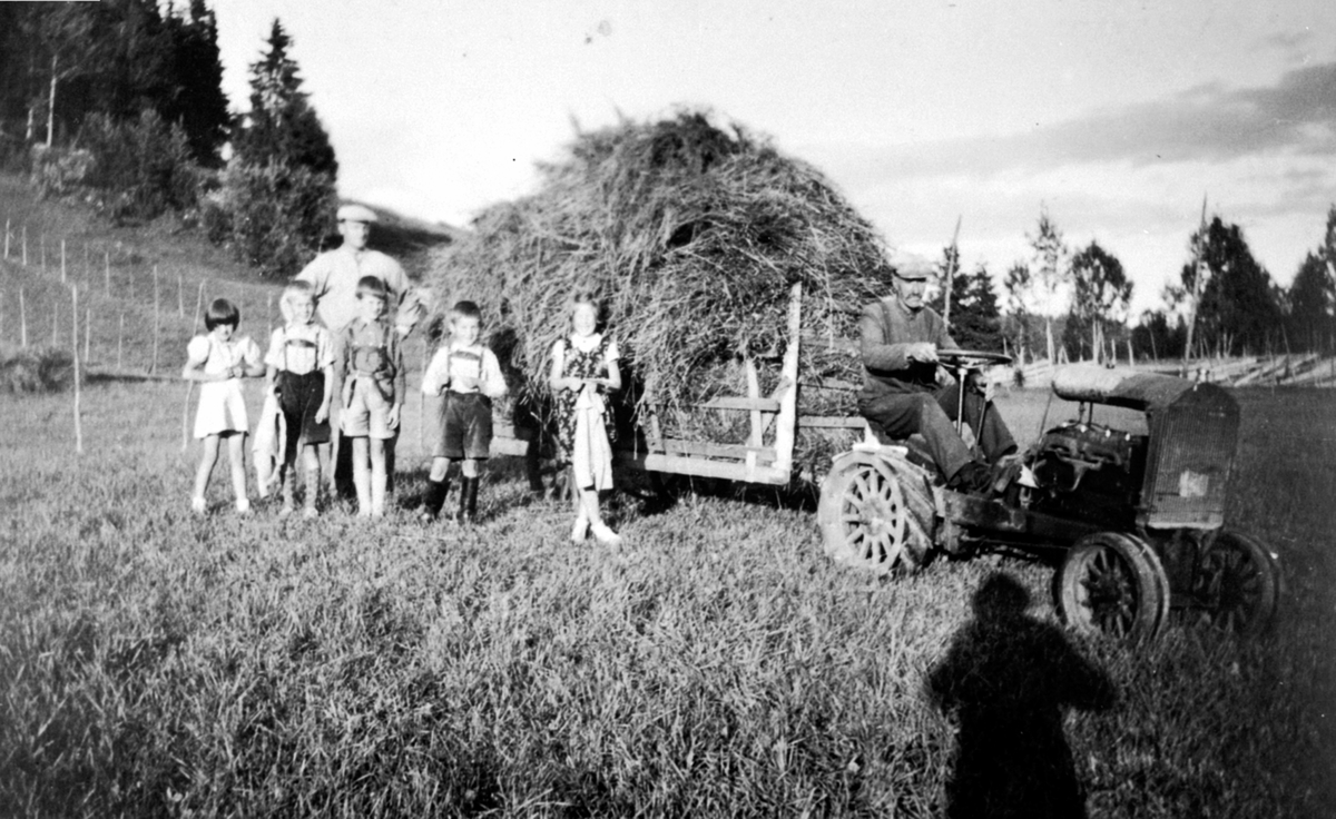 Høyonn. Ole J. Haug på sin selvbygde traktor med høylass. Fem barn. Bak er Bernt Aaseth, Brøttum, Ringsaker.