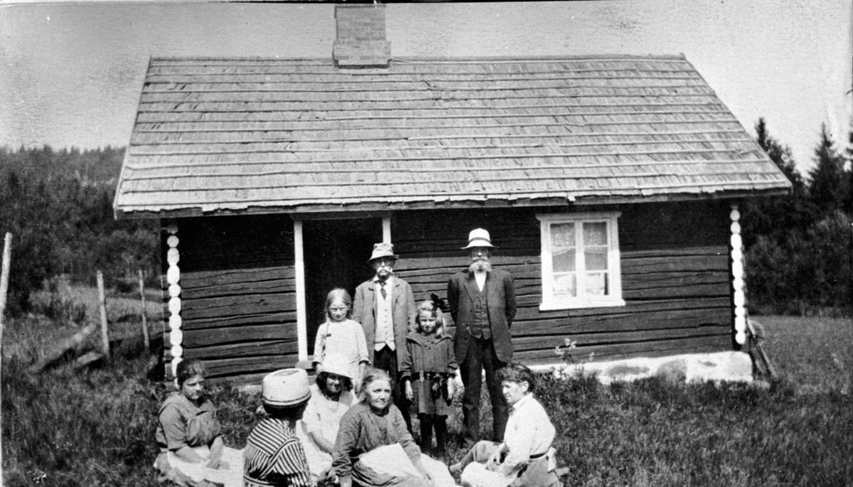 9 personer utenfor Stensrudstua på Vien, Helgøya. Bak fra høyre er Olaus Narmo (1861-1950), Karen Marie Regius (tysk), Karl Olsen, Johanne Vien. Sittende fra høyre er Kikki Olsen, Marie Narmo, ukjent, ukjent, Olga Narmo f.1896.