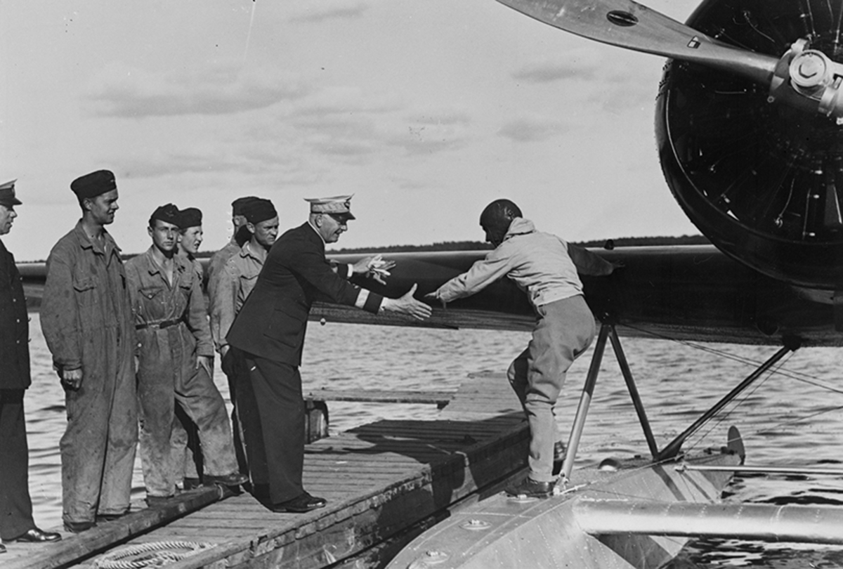 Anne Morrow Lindbergh stiger över från sjöflygplanet Lockheed 8 Sirius till brygga på F 2. På bryggan finns två högre befäl och fem män, flygvapenpersonal.