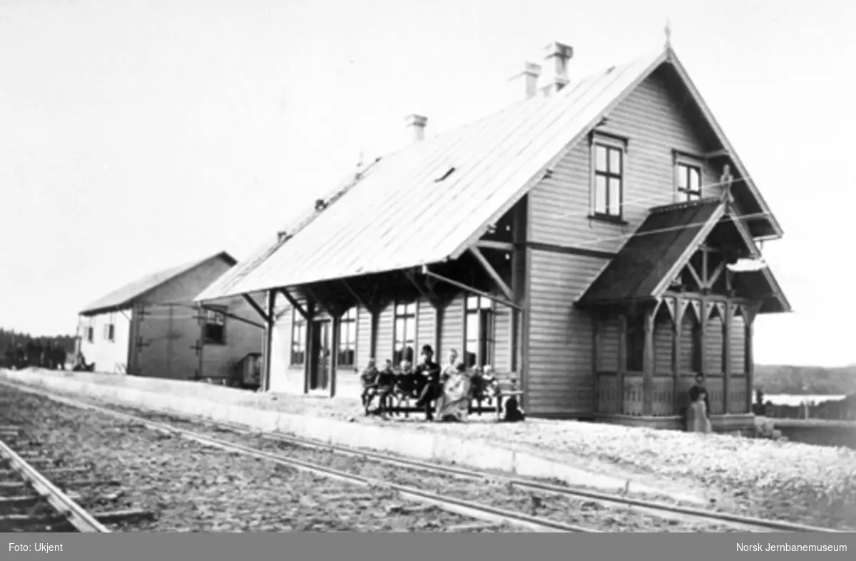 Prestebakke stasjon med stasjonsbygning og uthus; en familie sitter på benken på plattformen