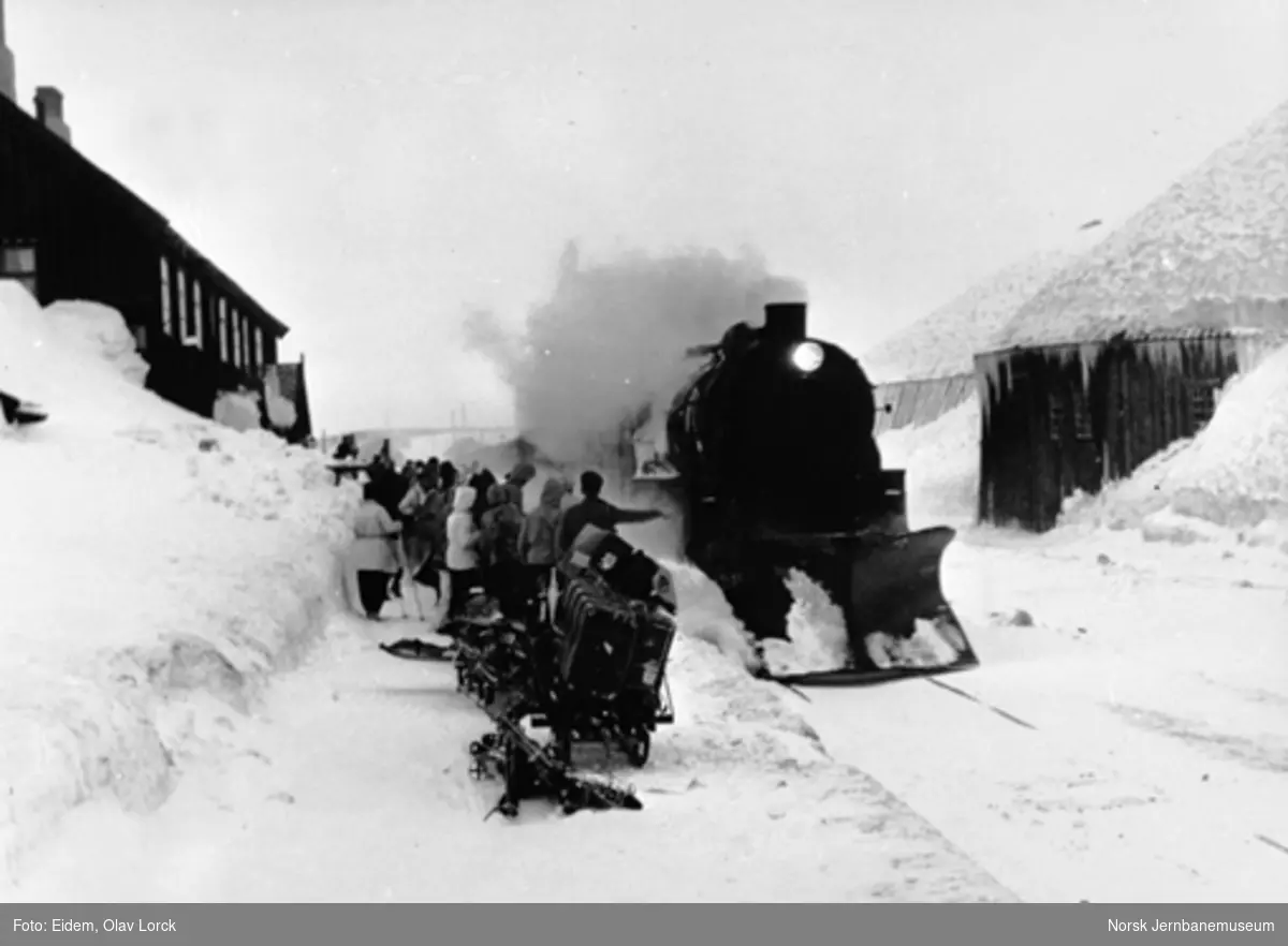 Damplokomotiv ankommer Finse stasjon med østgående persontog; reisende venter på plattformen