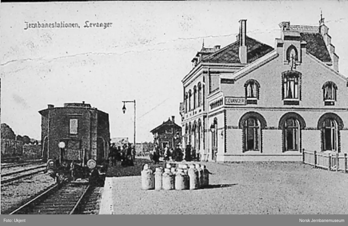 Levanger stasjon med stasjonsbygningen, reisende og tog i spor 1