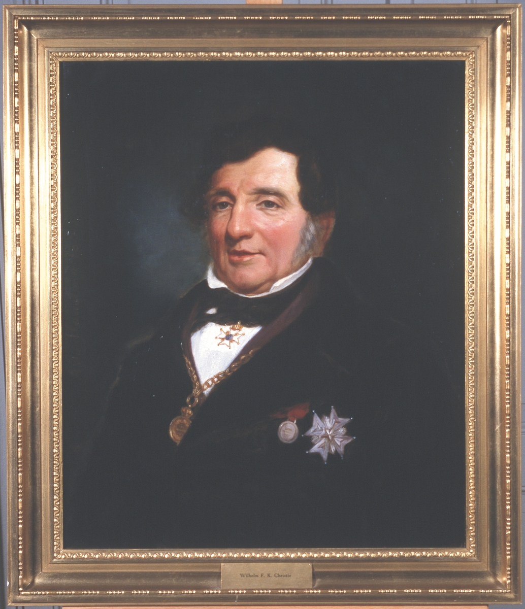 Portrett av Wilhelm F. K. Christie. 
Sort dress, sort sløyfe, hvit skjorte.  Mørkt hår. 2 ordener, 2 medaljer, klokke i kjede rundt halsen.