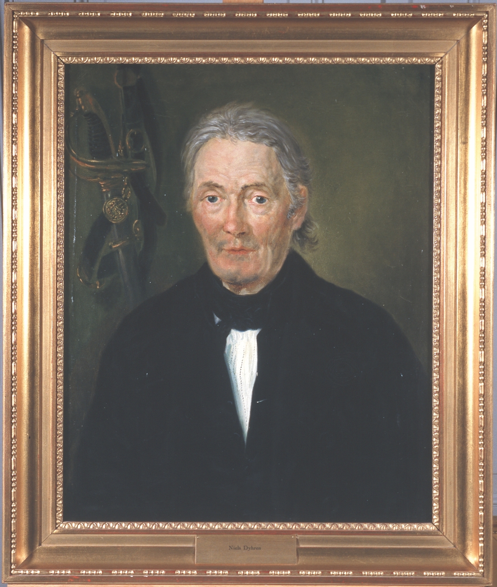 Portrett av Niels Dyhren. Mørk drakt, hvit skjorte, svart halsbind. Kårde i bakgrunnen.