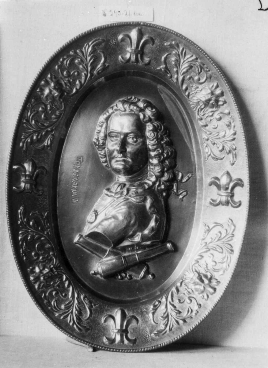 Messing. Ovalt, i bunnen Tordenskjolds brystbilde i relieff, derunder 2 korslagte lavetter, border og franske liljer, akantus og løvemasker.