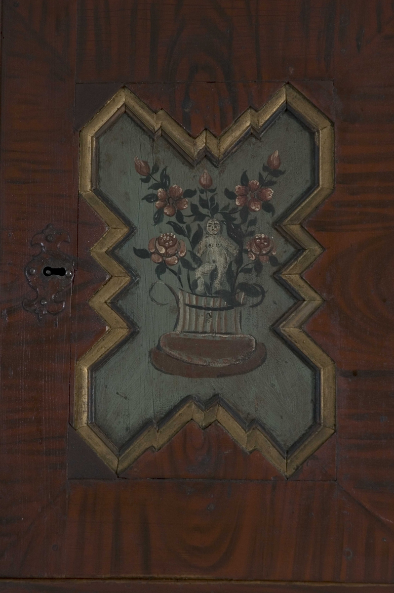 Doble dører oppe, to skyvedører på midten, en dør nede og to skuffer. Malte moriver: to adelsmenn og to blomster med nakne figurer oppi. Samson og løven på nedre skapdør. Marmorering i nisjen. Skyvedørene er dekorert med hester, kuer og geiter samt hus og en kirke.