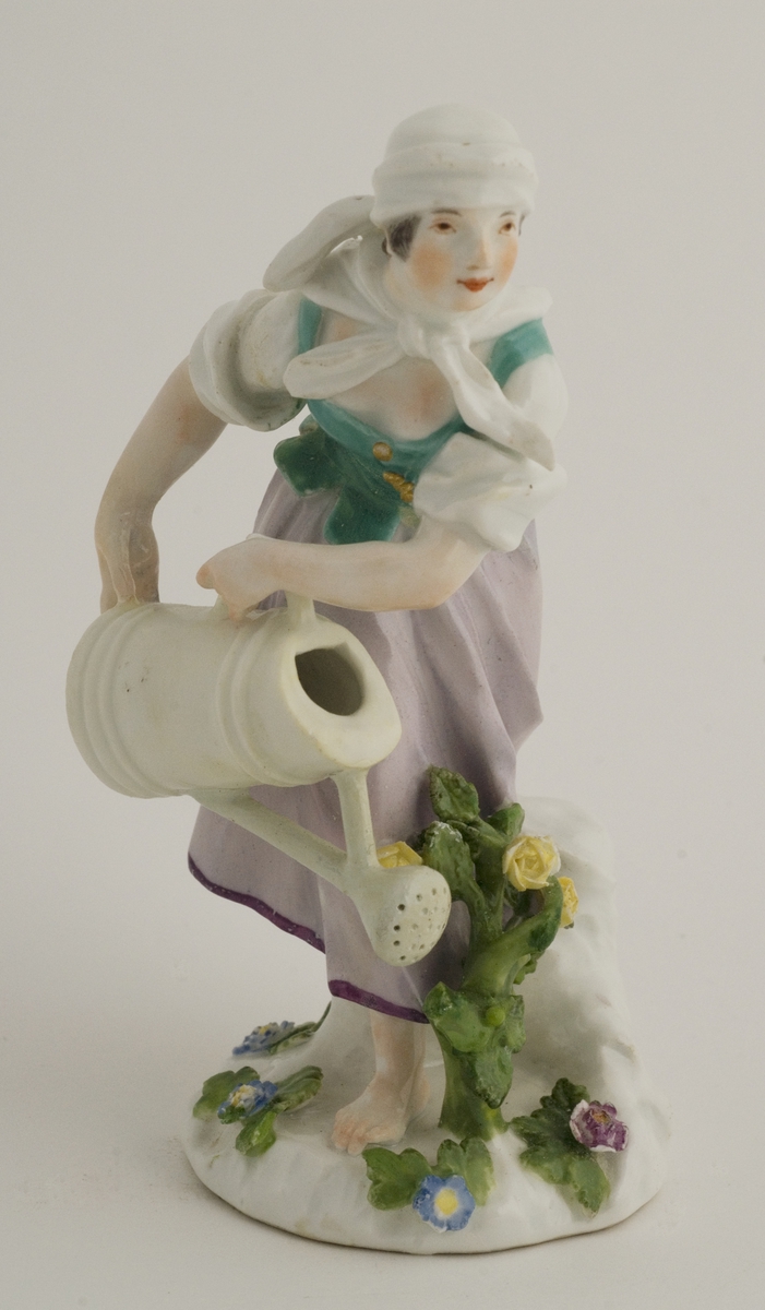 Figur, porselen, pike i violett skjørt, grønt lliv, vanner med hvitt krus. Merket med korslagte sverd på sokkelen.