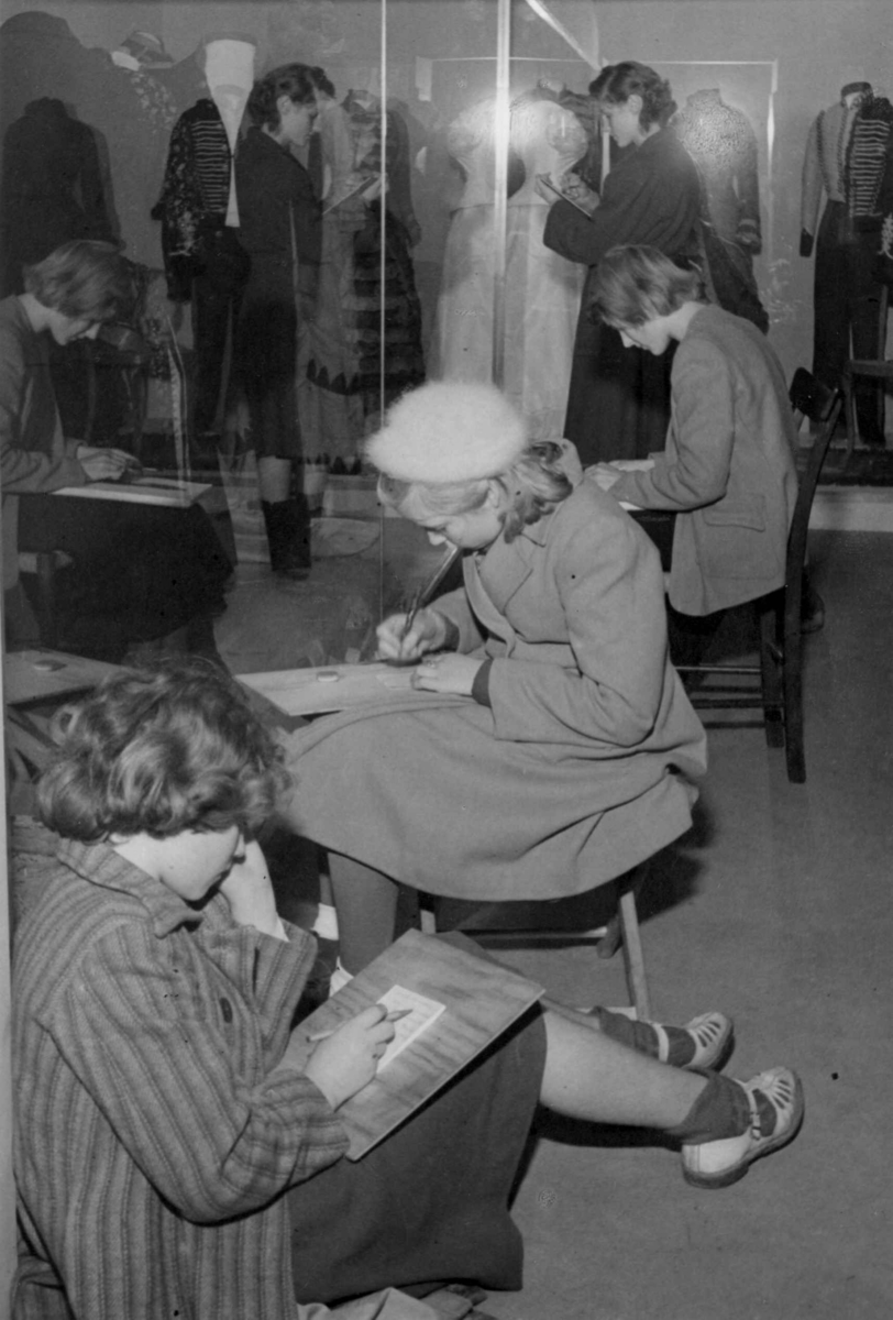 Skolejenter tegner i bysamlingen på Norsk folkemuseum, rom for drakter, etter 1950.