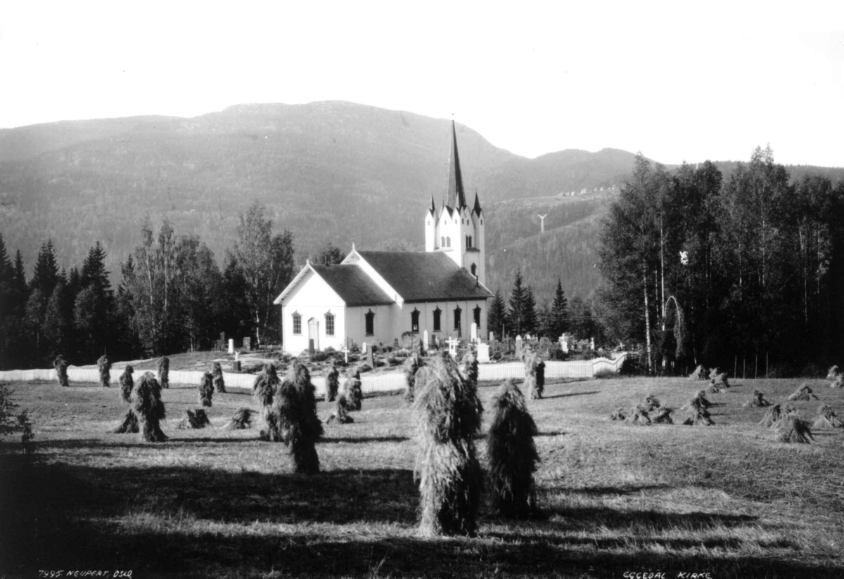 Eggedal kirke, Sigdal, Buskerud. 1930. Landskap. Kornstaurer og gravsteiner. Skog og fjell i bakgrunnen.