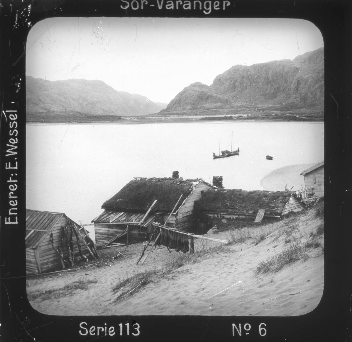 Grense Jakobselv, Sør-Varanger, Finnmark, ved Jakobsviken. I forgrunnen gårdsbebyggelse, fiskegarn tørkes.
Motivet har nr.6 i lysbildeforedraget kalt  "I lappernes land - Sør-Varanger", utgitt i Nerliens Lysbilledserier, serie nr 113. 