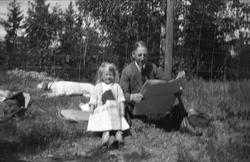 En mann og en jente sitter med hver sin avis ved et gjerde. 