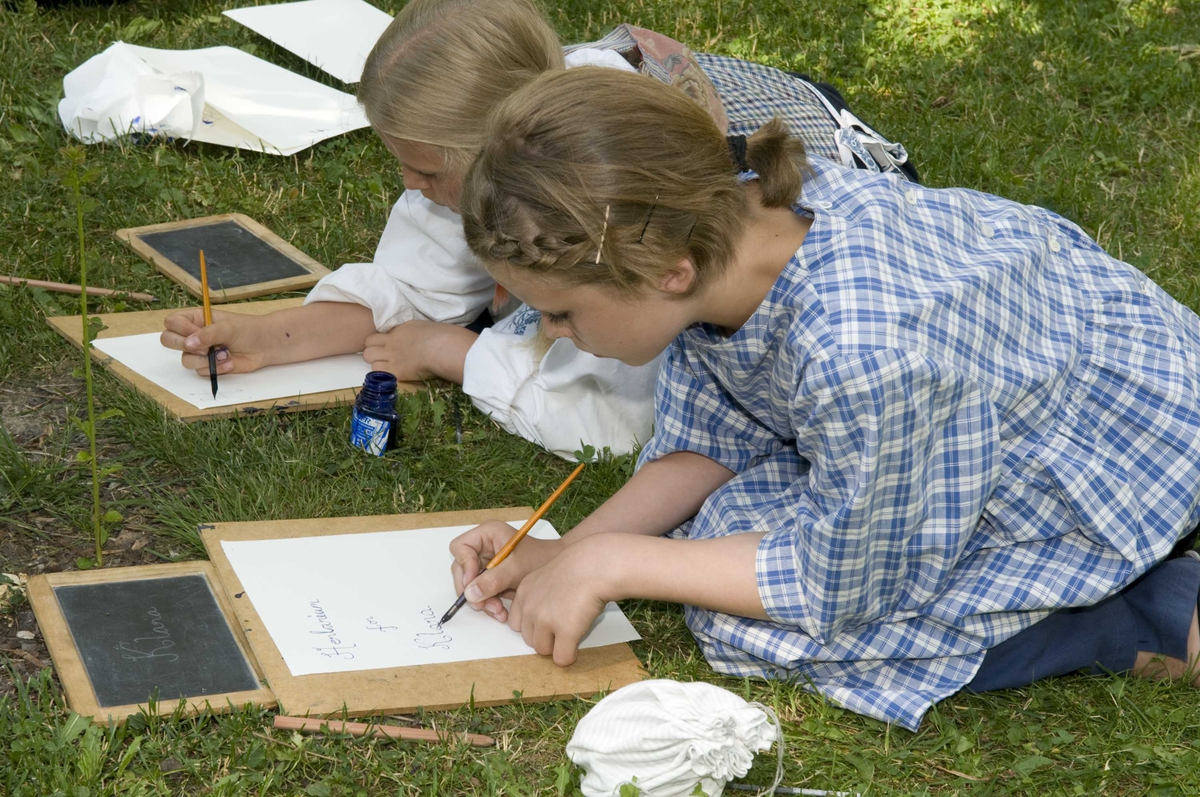 Ferieskolen uke 27, 2009.
Undervisning foregår utendørs, barna lærer å skrive med blekk.
