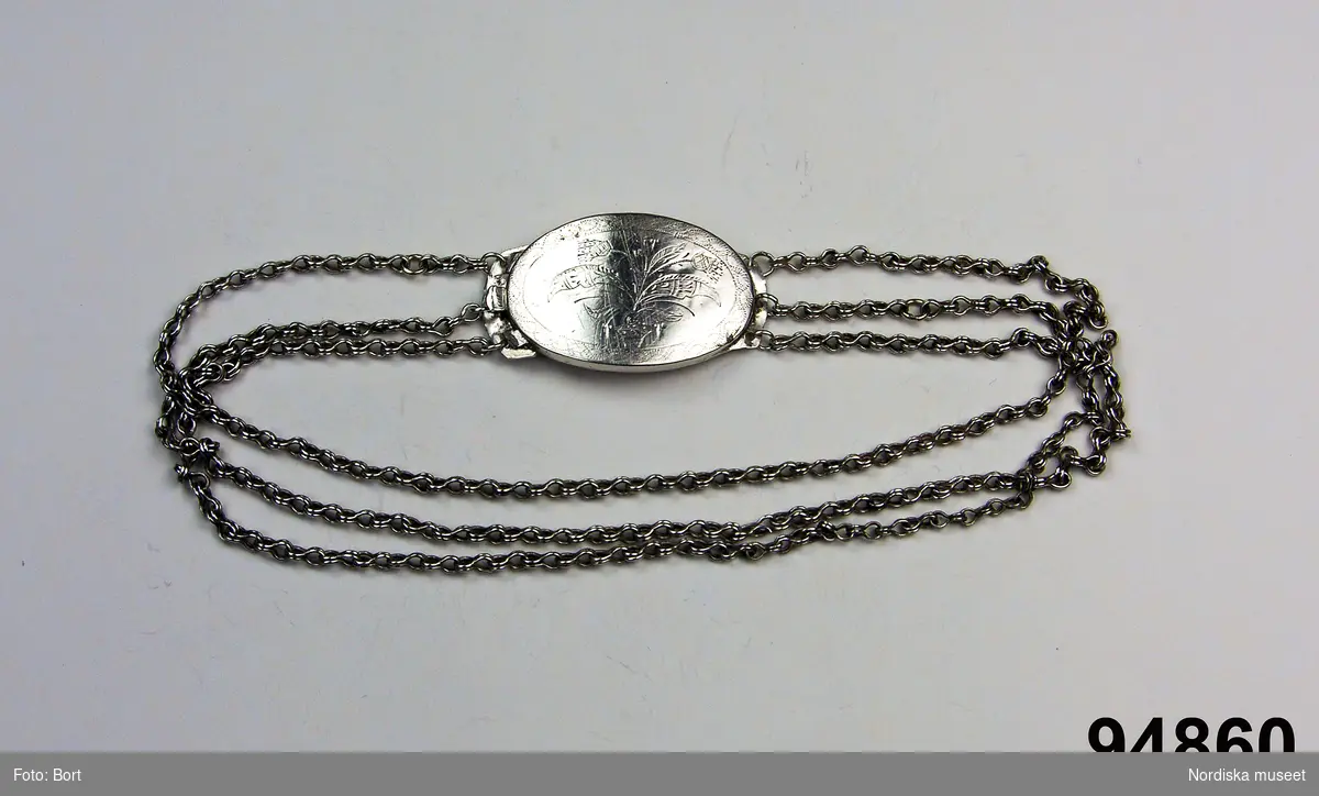 Ovalt lås av silverplåt , med graverad och trembolerad  blomdekor. Tre Tre halskedjor. Stämpat POS. Okänd silversmed
/Berit Eldvik 2006-12-04

