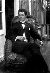 Mann sittende i stol på veranda. Avfotografert(?)