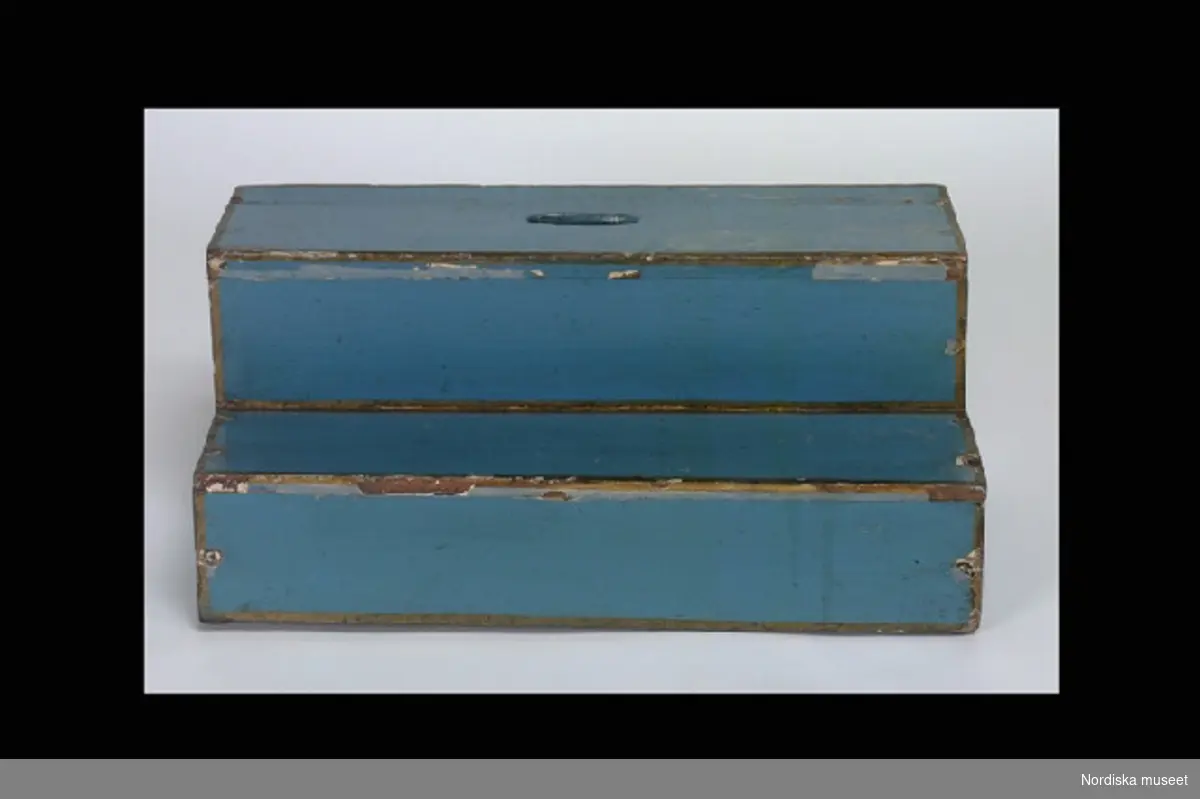 Inventering Sesam 1996-1999:L 110  B 45  H 215 (cm)
Dockskåp i fyra våningar (a), rokoko, av furu, målat i blått med förgyllda lister, uppdraget krön och avfasade hörn. Glasad och spröjsad dörr. Förgyllda rokokobeslag och springlås, pinnhängen.
b+) Löst underrede med låda på 6 st svängda ben. 
c) Spis, öppen härd, kvadratisk form, av gråmålat trä.
d) Fotpall (sekundär), rektangulär, av blåmålad furu med guldkanter, två steg, övre trappsteget med ovalt urtag.
e) Nyckel.
1:a våningen:
Kök med målat brunt stengolv. Porslinskök med målat grönt stengolv. Gråmålade väggar.
2:a våningen:
Sovrum och gemak, grönmålade väggar med rokokoornamentik i guld. Sal, rosamålade väggar med  rokokoornamentik i guld. Målade parkettgolv i olika utförande.
3:e våningen:
Väggar med målad bröstpanel och landskapsmålningar. Svart- och vitrutigt målat golv.
4:e våningen:
Målad bröstpanel. Rödmålad vägg med gul rokokoornamentik. Målade parkettgolv.
Har tillhört Maria Catharina Falck (1752-1801), g. med Carl Fredrik Ekerman, justitieborgmästare i Stockholm.
Möbler, husgeråd m.m. från 1700-talets mitt - 1800-talets mitt, se inv nr 151.826-152.006. Fajansservis (inv.nr 114.397-114.400) Rörstrand, sign. 1746. Porträtt föreställande bl a fam. Falck och Ekerman. Skåpet har tidigare varit målat i vitt med förgyllda lister, jfr foto från 1909 på äldre katalogkort.   
  
Anna Womack 1996