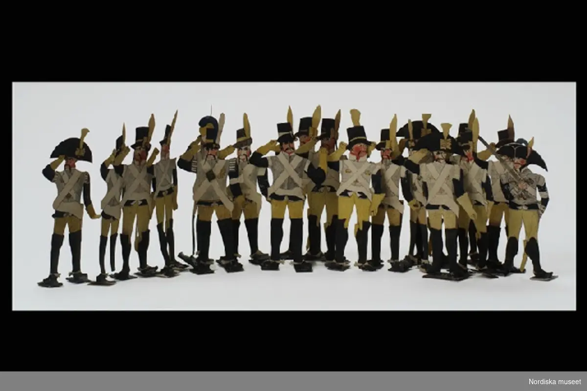 Inventering Sesam 1996-1999:
H 11 cm
19 st soldater av papper, målade med vattenfärg. Klädda i svensk uniform, blå jacka, harnesk, gula byxor, sadelväska med tre kronor, svarta höga stövlar, hög hatt. Fyra soldater med trekantig hatt. Påteckningar på fotplattorna "Asp", "Ek", "Berg" mm.
Tillhör dockteater se inv 191.511. Har brukats på Lilla Främsbacka, Stora Kopparbergs sn, Dalarna.
Birgitta Martinius 1996