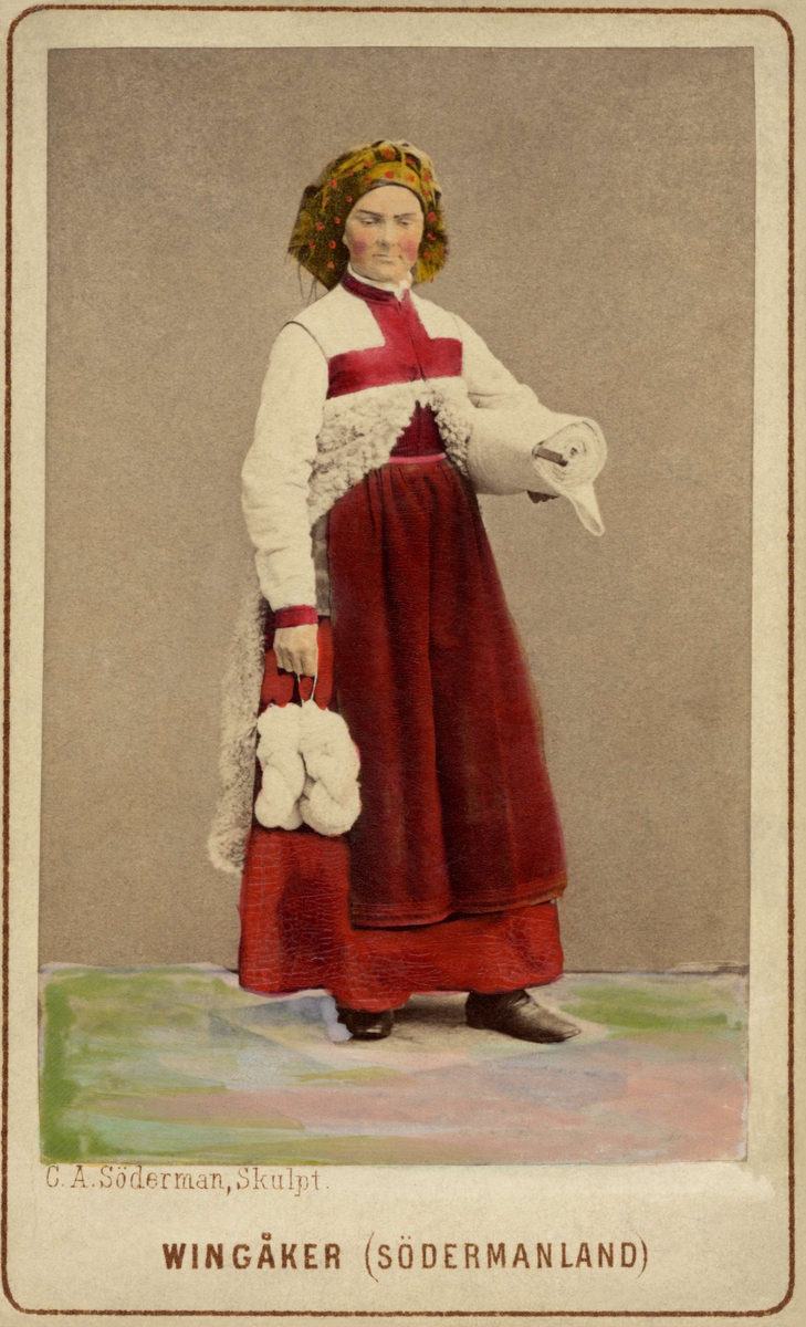 Kvinna i sockendräkt från Vingåker, Södermanland. Dräktdocka med huvud skulpterat av C A Söderman, visad på världsutställningen i Wien 1873. Handkolorerat fotografi.