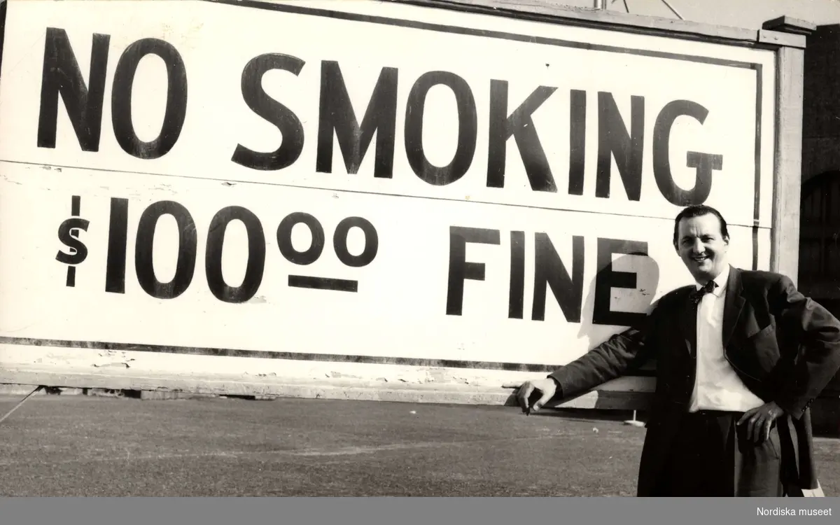 KW Gullers poserar framför skylt med texten "No Smoking - $100 Fine"