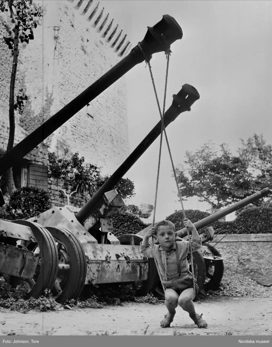 Italien. Pojke gungar i rep upphängt i röret på en tysk kanon från andra världskriget.