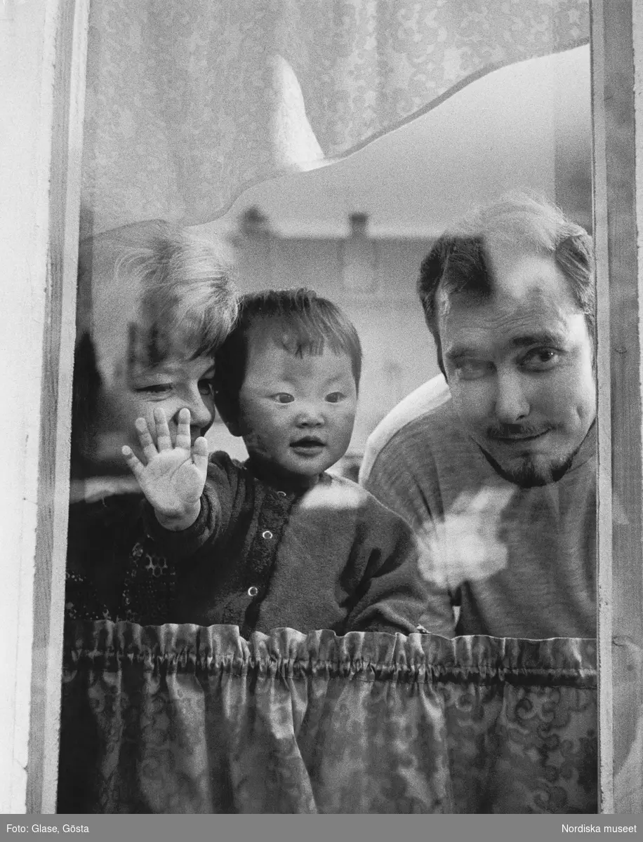 Adoptivbarn. Mor, far och barn tittar ut genom fönster.