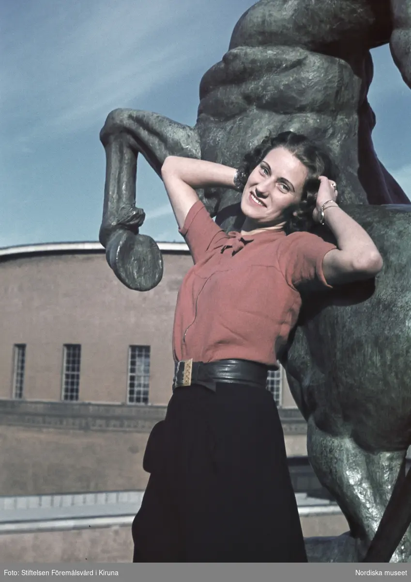 Kvinna iklädd röd blus och svart kjol. I bakgrunden Sigrid Frimans skulptur Kentauren från 1939 i Observatorielunden, Stockholm