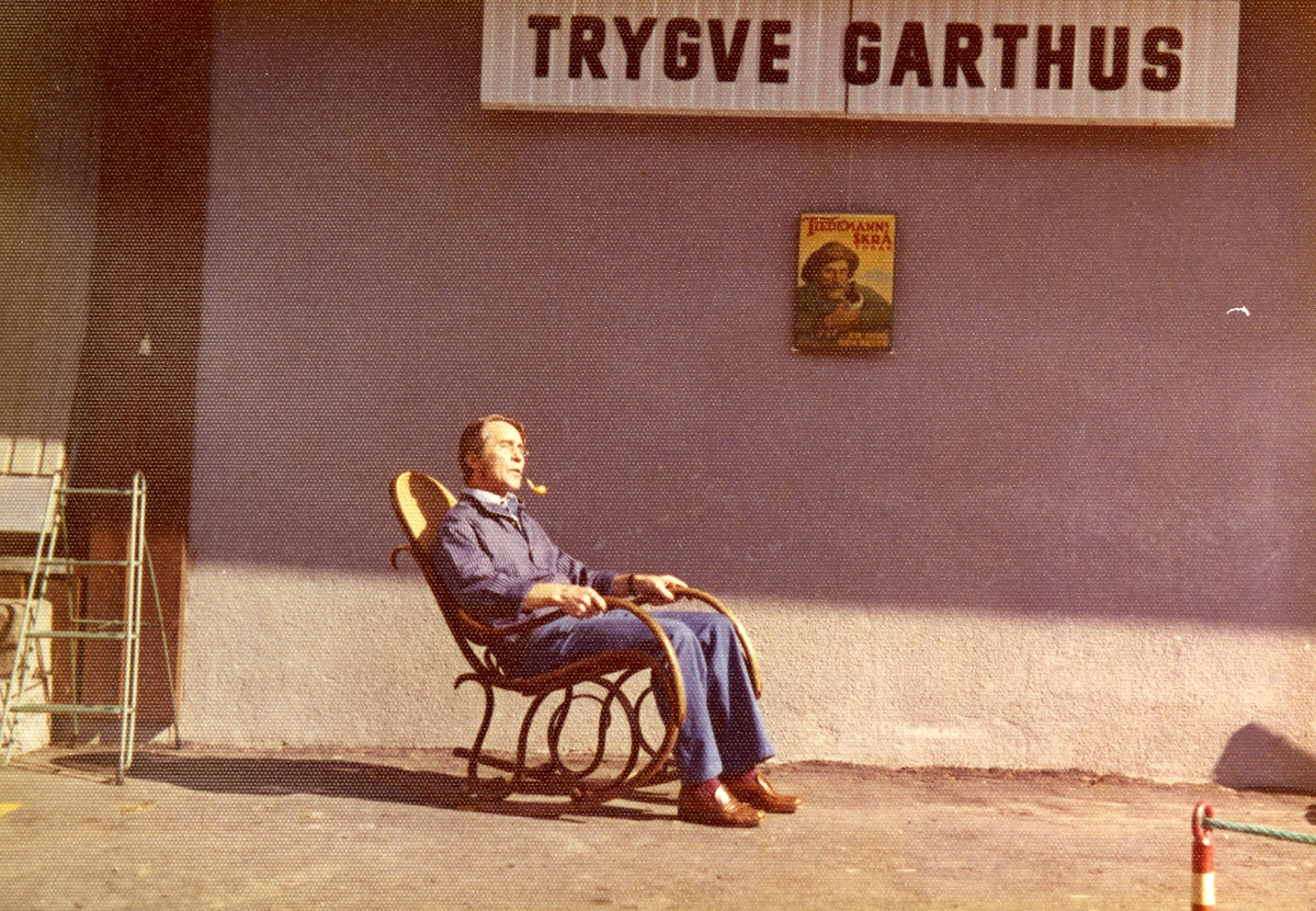 Kjøpmann Trygve Garthus røyker pipe utenfor forretningen ved samme navn - Trygve Garthus.