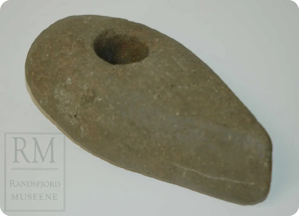 Oval øks av stein, med definert og slipt egg i ene enden. Skafthull i den enden som er avrundet. 