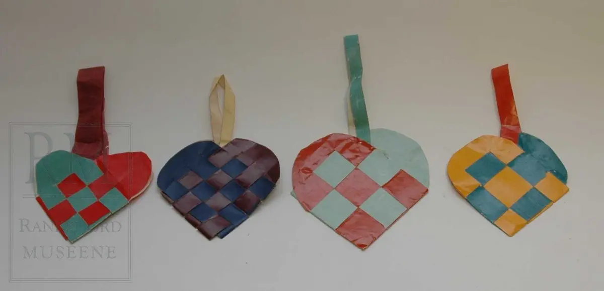 Papir, hjerteformet, 9 ruter, flettet. Lange hjertebuer. Hank i silkepapir er limt på. 

Foto: Nr. 1 fra venstre
