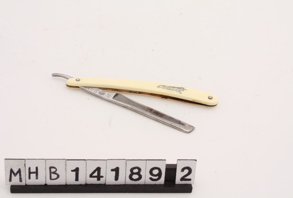 Barberkniv i  to deler, der knivbladet kan legges inn i skaftet. Barberbladet er rektangulært i skjæredelen, med spisst knivblad med skrå tupp. Knivbladet ender i et skaft som er skrudd fast til et større plastskaft. Plastskaftet består av to deler som er skrudd sammen, slik at det er plass til knivbladet inni.
