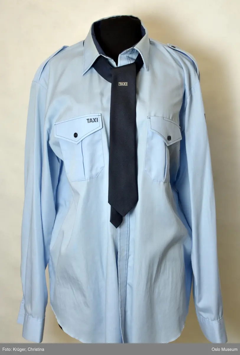 Uniform for Taxi inspektør. Taxi uniformen består av lyseblå skjorte med Taxi merke, et blått slips med Taxi logo, en bukse med PELLY merke og en blå jakke i str. 46 og en lue/hatt.