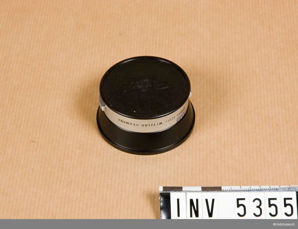Motljusskydd för Leitz optik med spår avsedda för med speciell klämmekanism fasthållna motljusskydd. Skyddet är avsett för brännvidderna 35 och 50 mm med ljusstyrka 1:2-1:3,5. Av svart och matt vitmetall. Mått 25x57 mm, koniskt. Avsett för objektiv med filtergänga d:42 mm, kallad E 39.   Nyskick.Objektivlock i svart plast, att användas när motljusskyddet, för att spara utrymme, monteras bakvänt på objektivet.Emballage av kartong i två delar, grönt, svart, brunt; defekt.