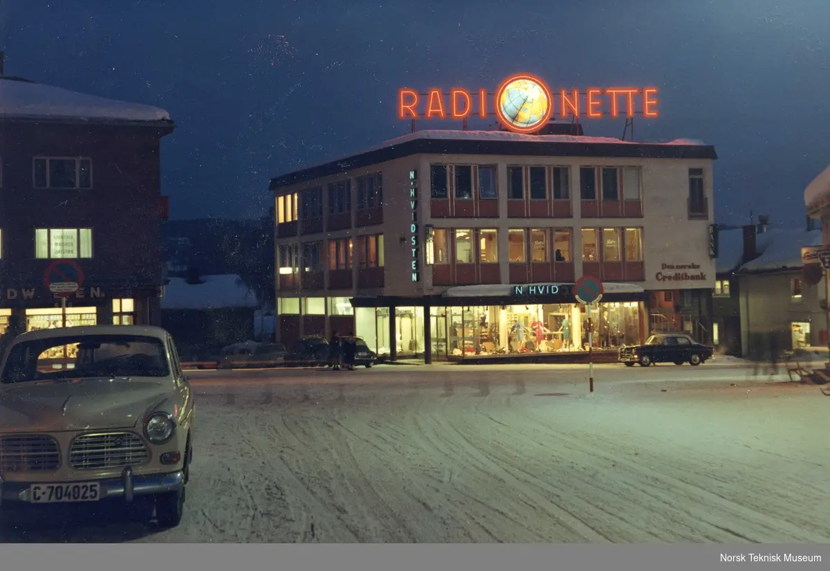 Radionette, lysreklame, Storgata 6, Kongsberg med Volvo Amazon i forgrunnen, omkring 1970