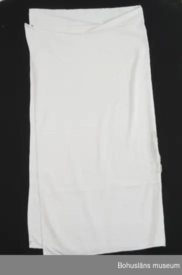 Stor kvadratisk handduk av vit frotté med en invävd figur strödd över tyget.
Slitna kanter, revor, flera hål.