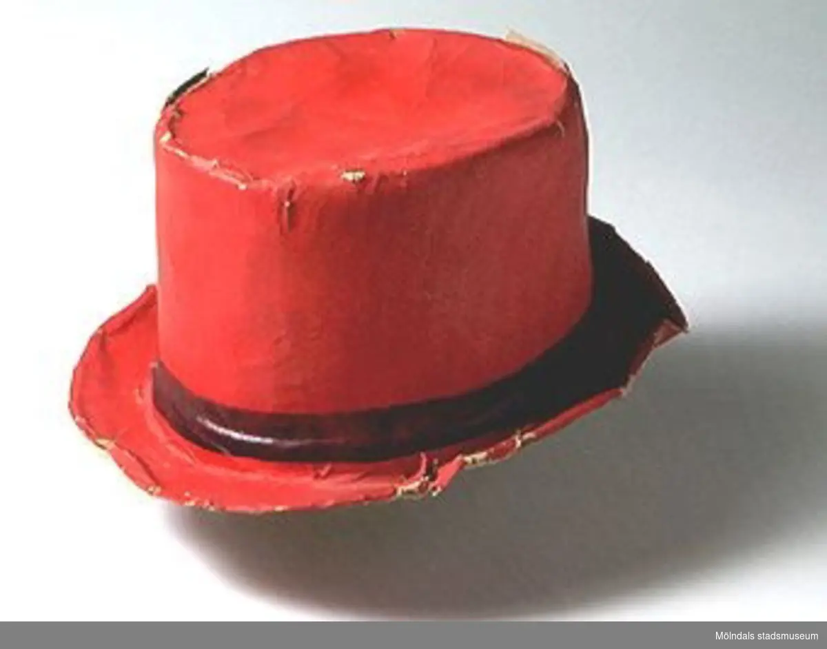 Röd cylinderhatt med påmålat brunt brätte.