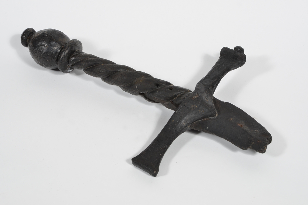 Skulpturdetalj, handfäste/kavel till svärd. tillhörande människofigur. Avlångt och spiralornerat, med en profilerad svärdsknapp i ena änden. I den andra änden finns ett urtag för svärdets parerstång.

Handfästet är ihopmonterat med den separat snidade parerstången och svärdsklingan, se fyndnummer 01456. Klingans tånge är fastsatt i handfästets urtag med en recent pinne eller liknande, vilken är instucken genom ett av två hål i handfästet.

Svärdsknappen är något skadad. I övrigt är skulpturdelen välbevarad, förutom mindre sprickor.

Det finns synliga spår av guld på skulpturdelarna (1997).